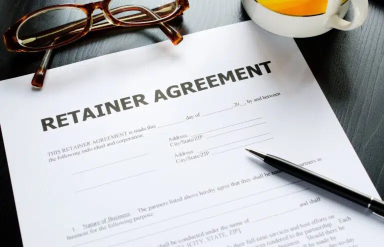 Retainer agreement document with pen, glasses, and coffee cup on a desk, representing the benefits of retainer agreements with a lawyer, especially in family law cases in Ontario.