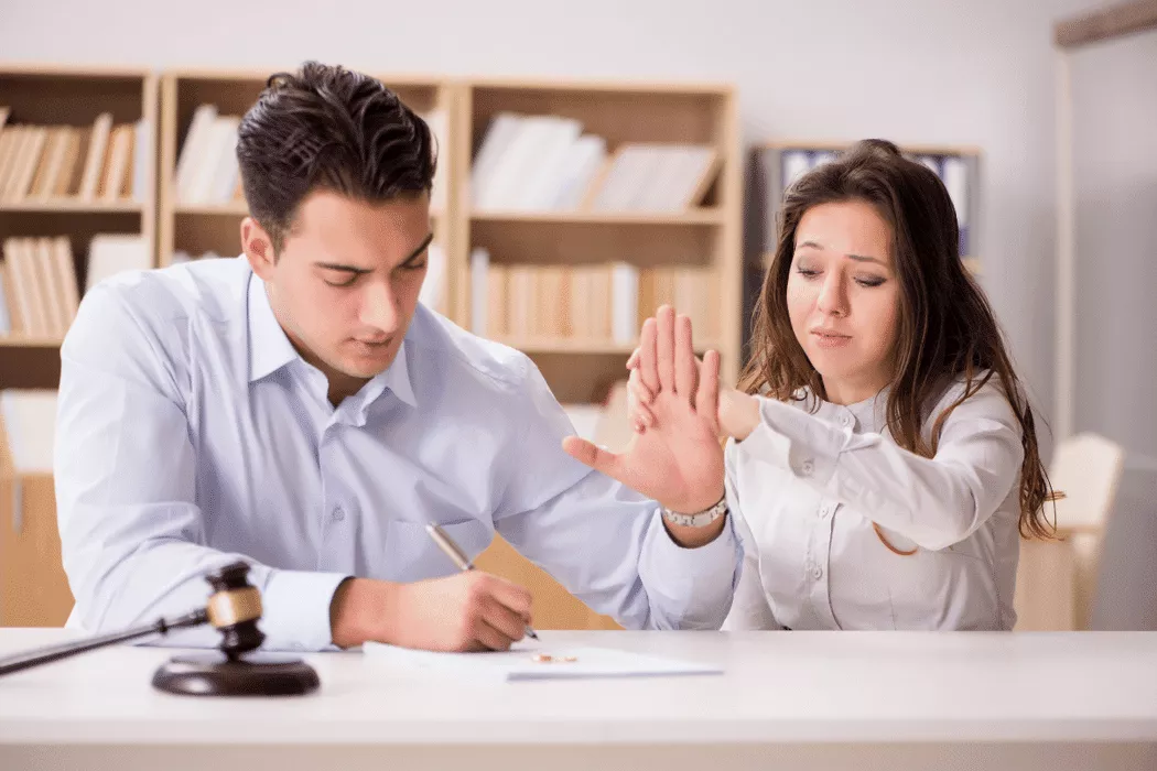 A woman in distress reaching out to a man who is refusing and signing documents at a desk in a legal office setting, symbolizing family law issues addressed by Nussbaum Family Lawyers in Toronto.
