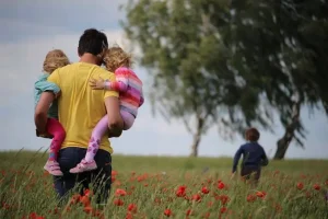 A father walking through a field of red flowers carrying two young children, symbolizing family care and support, reflecting the services of Nussbaum family lawyers in Toronto.