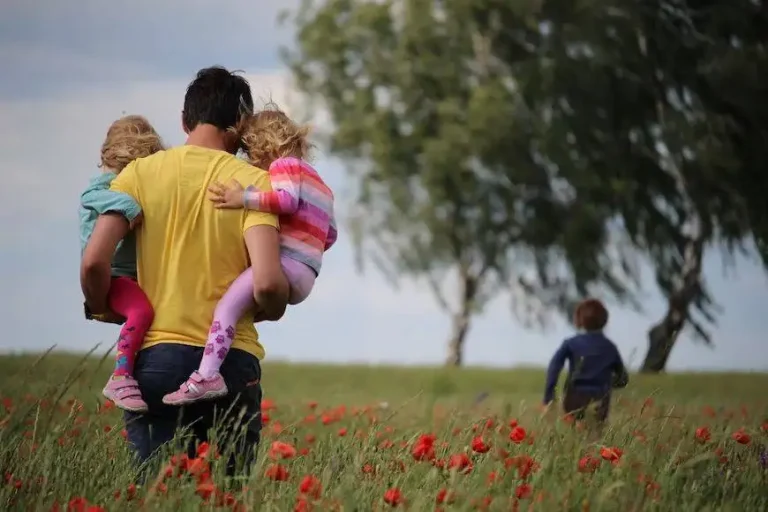 A father walking through a field of red flowers carrying two young children, symbolizing family care and support, reflecting the services of Nussbaum family lawyers in Toronto.