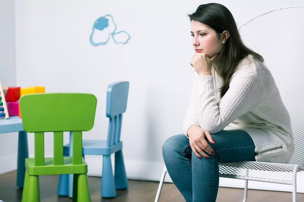 Thoughtful woman sitting alone in a waiting area with colorful children's chairs and toys, representing a family law consultation setting in Toronto with Nussbaum family lawyers.